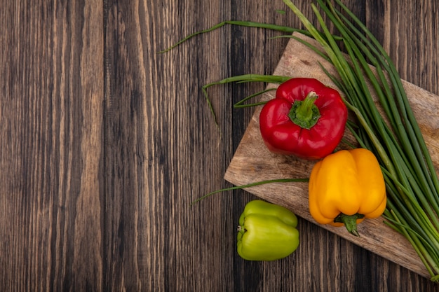 Bovenaanzicht kopie ruimte gekleurde paprika met groene uien op een snijplank op houten achtergrond