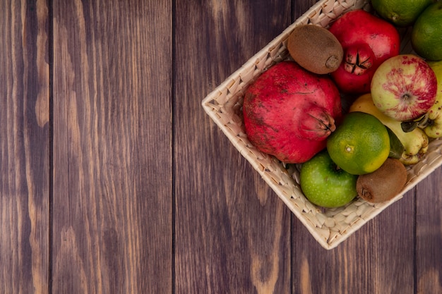Bovenaanzicht kopie ruimte granaatappels met mandarijnen appels peren en kiwi in een mand op houten muur