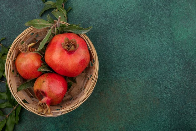 Bovenaanzicht kopie ruimte granaatappels met takken in een mand op een groene achtergrond