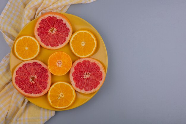 Bovenaanzicht kopie ruimte grapefruit plakjes met stukjes sinaasappel op een gele plaat met een gele geruite handdoek op een grijze achtergrond