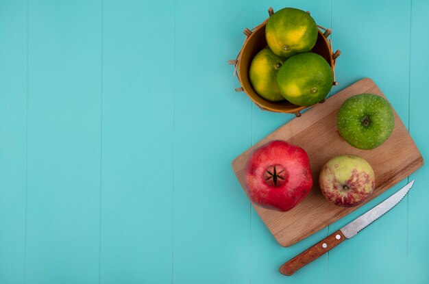 Bovenaanzicht kopie ruimte veelkleurige appels op een snijplank met granaatappel en mandarijnen in een mand op een blauwe muur