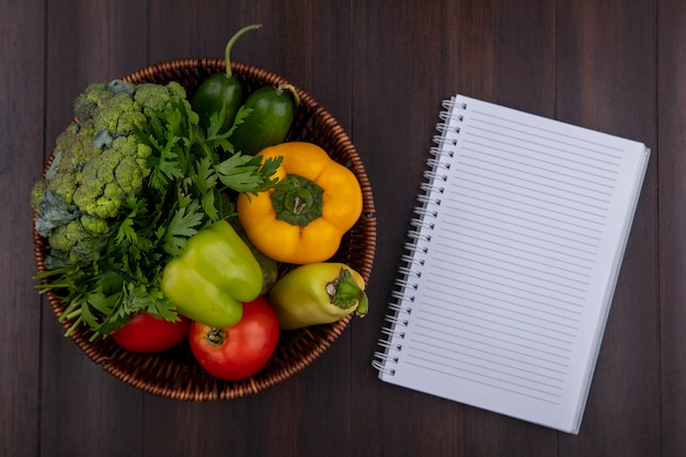 Bovenaanzicht kopie ruimte voorbeeldenboek met paprika, peterselie en tomaten in een mand op houten achtergrond