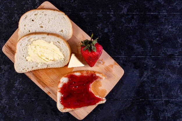 bovenaanzicht kopieer ruimte sneetjes brood en boter met een sneetje brood met jam aan boord met aardbeien