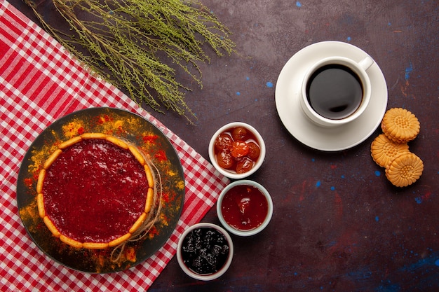 Bovenaanzicht kopje koffie met heerlijke dessertcake koekjes en fruitjams op donker bureau zoet fruit koekjeskoekje zoet