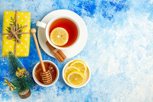 Bovenaanzicht kopje thee kerstboom cake op bord schijfjes citroen honing gele geschenkdoos op blauwe tafel vrije plaats