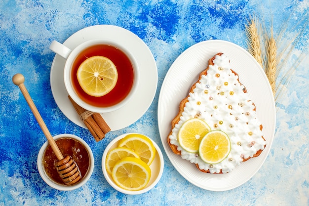 Bovenaanzicht kopje thee kerstboom cake op plaat citroen schijfjes honing in kom op blauwe tafel