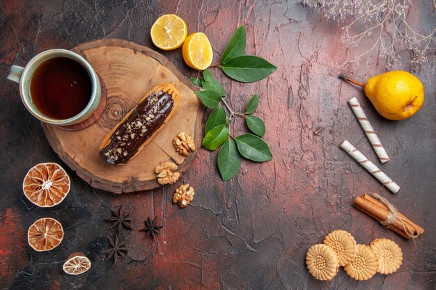 Bovenaanzicht kopje thee met eclair en koekjes op de donkere tafel zoete koektaart