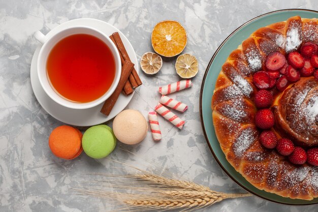 Bovenaanzicht kopje thee met Franse macarons en aardbeientaart op licht-wit oppervlak