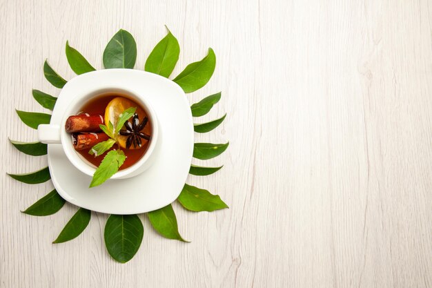 Bovenaanzicht kopje thee met groene bladeren op witte bureau kleur thee fruit ceremonie