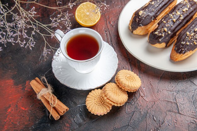 Bovenaanzicht kopje thee met koekjes en eclairs op donkere vloer suiker thee koekje zoet