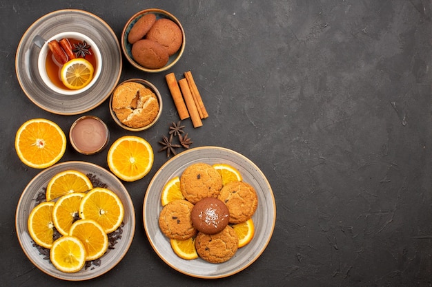 Bovenaanzicht kopje thee met koekjes en vers gesneden sinaasappels op het donkere oppervlak zoete thee fruitkoekje