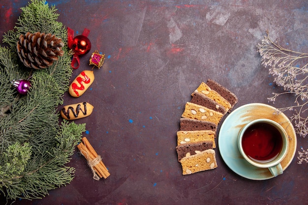 Bovenaanzicht kopje thee met plakjes cake en koekjes op donkere ruimte