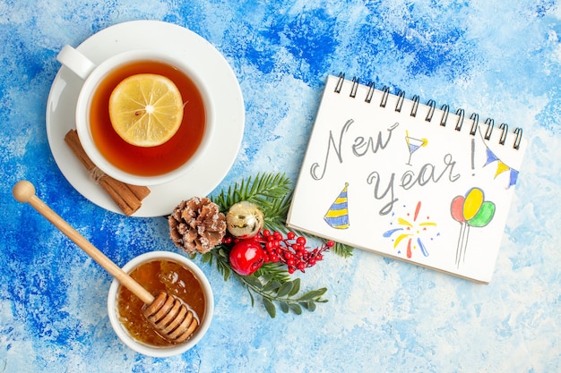 Bovenaanzicht kopje thee nieuwjaar geschreven op notebook honing in kom op blauwe tafel