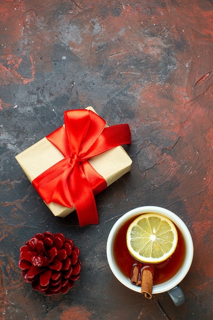 Bovenaanzicht kopje thee op smaak gebracht door citroen en kaneel kerstcadeau rode dennenappel op donkerrode tafel