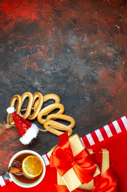 Bovenaanzicht kopje thee op smaak gebracht door citroen en kaneel mini kerstmuts op rood tafelkleed ovale bagels cookies op donkerrode tafel