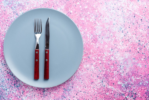 Bovenaanzicht lege plaat blauw gekleurd met vork en mes op roze bureau kleur foto plaat eten bestek