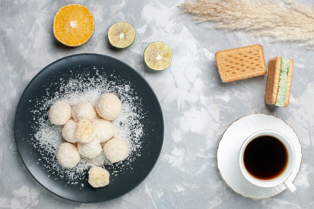 Bovenaanzicht lekker kokos snoepjes met kopje thee op wit