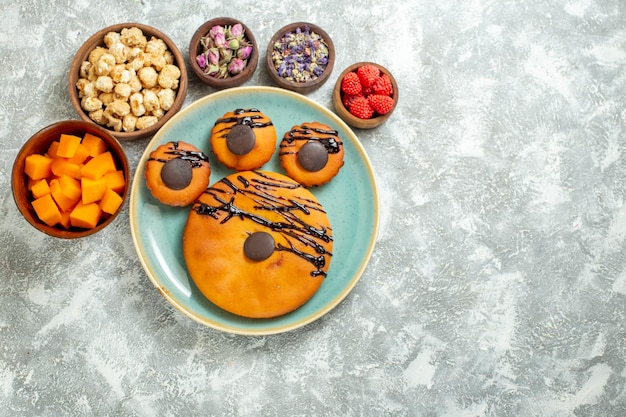 Bovenaanzicht lekkere cacaocakes met chocoladesuikerglazuur en bloemen op witte oppervlaktekoekje, zoete cake, dessertkoekjestaart