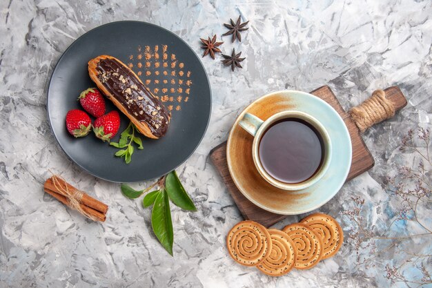 Bovenaanzicht lekkere choco-eclairs met kopje thee op een lichte biscuitdesserttaart