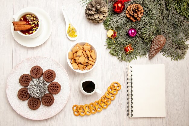 Bovenaanzicht lekkere chocoladekoekjes met kleine cacaocake en thee op het witte bureau