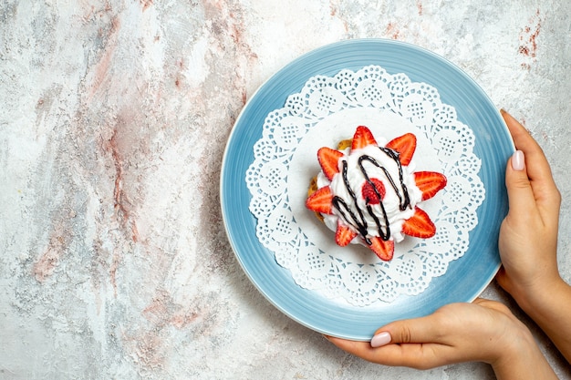 Bovenaanzicht lekkere kleine cake met room en aardbeien op wit