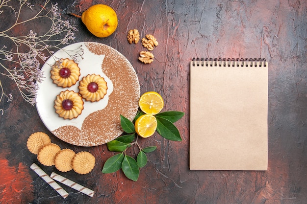 Gratis foto bovenaanzicht lekkere kleine koekjes met fruit op de donkere tafel suiker cake zoete koekje