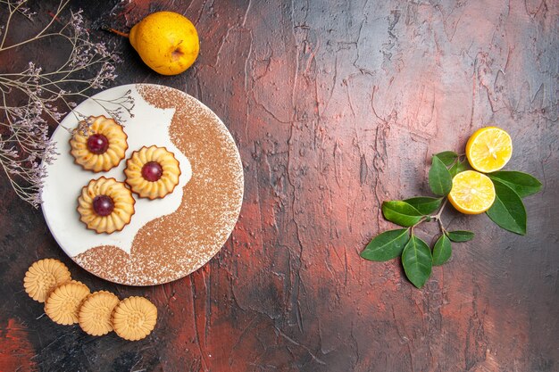 Bovenaanzicht lekkere kleine koekjes met fruit op donkere tafel cake zoete koekjessuiker