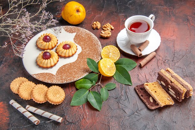 Bovenaanzicht lekkere kleine koekjes met kopje thee op de donkere tafel suiker cake zoete koekje