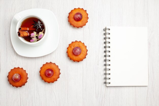 Bovenaanzicht lekkere kleine taarten met kopje thee op witte ondergrond dessert cookie biscuit thee taart taart