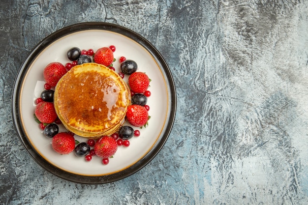 Bovenaanzicht lekkere pannenkoeken met fruit en honing op lichte vloer