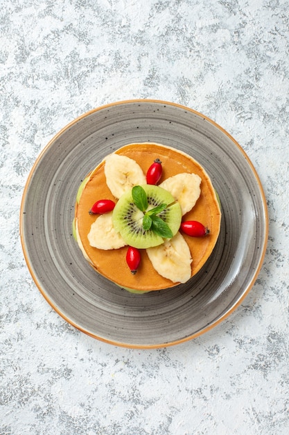 Bovenaanzicht lekkere pannenkoeken met gesneden fruit in plaat op wit oppervlak fruit zoet dessert suiker ontbijt kleur cake