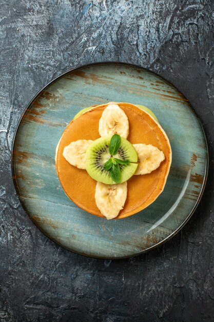 Bovenaanzicht lekkere pannenkoeken met gesneden kiwi's en bananen op donkere oppervlakte fruit zoete dessert kleur cake suiker