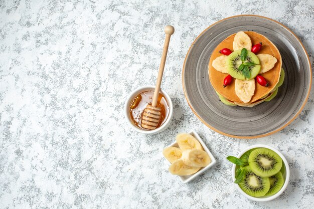 Bovenaanzicht lekkere pannenkoeken met honing en gesneden fruit op witte achtergrond fruit zoet dessert ontbijt kleur cake suiker
