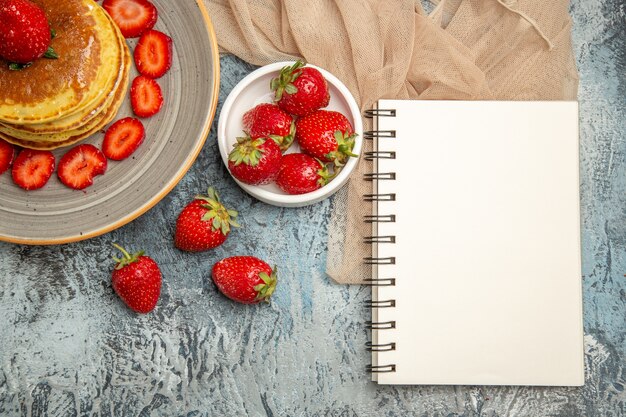 Bovenaanzicht lekkere pannenkoeken met verse aardbeien op een licht bureau zoet fruit