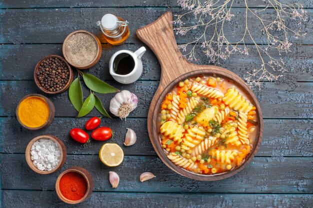 Bovenaanzicht lekkere pastasoep van spiraalvormige italiaanse pasta met kruiden op donkerblauwe bureaukeuken pastasoep kleurschotel diner