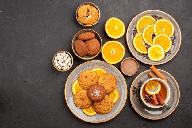 Bovenaanzicht lekkere zandkoekjes met verse sinaasappels en kopje thee op een donkere achtergrond, fruitkoekje, zoet koekje, citrussuiker