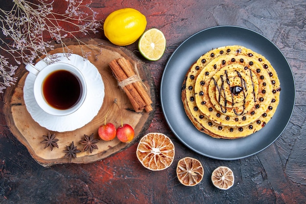 Bovenaanzicht lekkere zoete pannenkoeken met kopje thee op donkere ondergrond