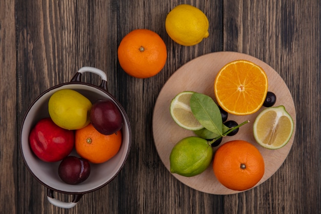 Gratis foto bovenaanzicht limoen helften met oranje helft op een stand met citroenen pruimen kersenpruim en perzik in een pan op een houten achtergrond