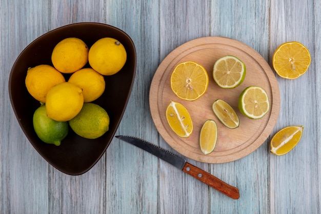 Gratis foto bovenaanzicht limoenen (lemmetjes) met citroenen in kom en wiggen op snijplank met mes op grijze achtergrond