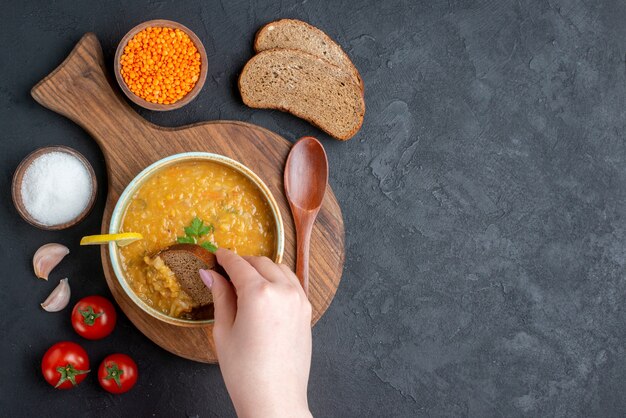 Bovenaanzicht linzensoep met zoute tomaten en donkere broodbroden op donkere ondergrond