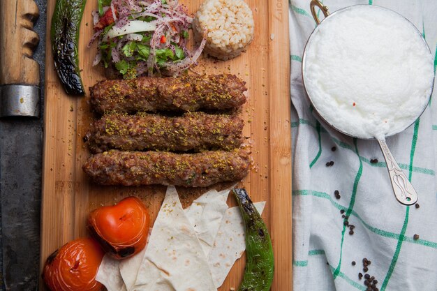 Bovenaanzicht lula kabab met gebakken groenten en gehakte ui en ayran en mes in snijplank