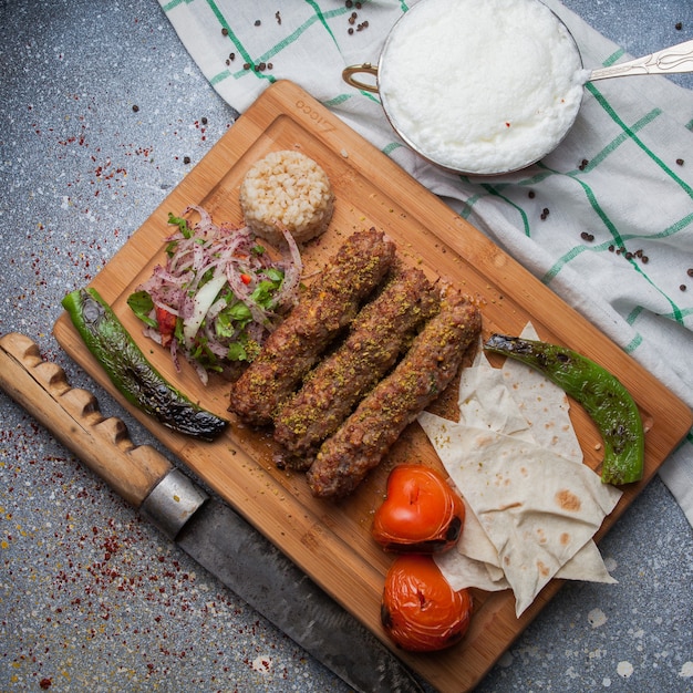 Bovenaanzicht lula kabab met gebakken groenten en gehakte ui en mes en ayran in snijplank