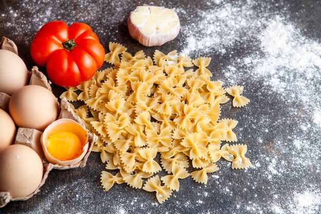 Bovenaanzicht macaroni met eieren, tomaten en knoflook op donkere gestructureerde achtergrond.