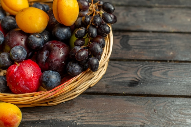 Bovenaanzicht mand met zacht zuur fruit zoals druiven abrikozen pruimen op het bruine bureau