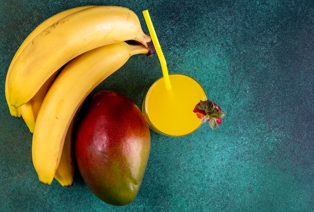 Bovenaanzicht mango met bananen en sinaasappelsap met een gele rietje op groen