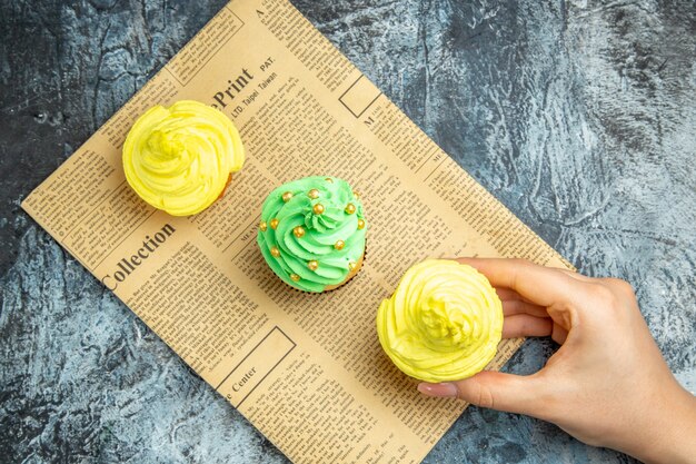 Bovenaanzicht mini cupcakes vrouwelijke hand cupcake nemen op krant op donkere ondergrond