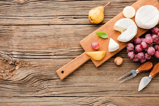 Gratis foto bovenaanzicht mix van gastronomische kaas op houten snijplank druiven en gebruiksvoorwerpen met kopie ruimte