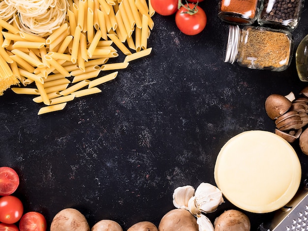 Bovenaanzicht mix van ongekookte rauwe pasta, spaghetti, macaroni naast champignons, kaas, tomatensaus, verse tomateos, kruiden en zonnebloemolie. copyspace beschikbaar