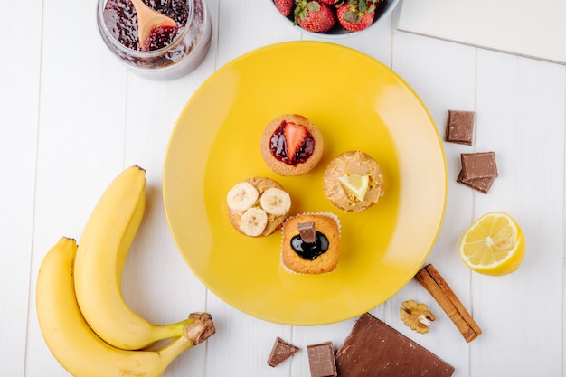 Bovenaanzicht muffins met bananen aardbeien chocolade en citroen op een gele plaat