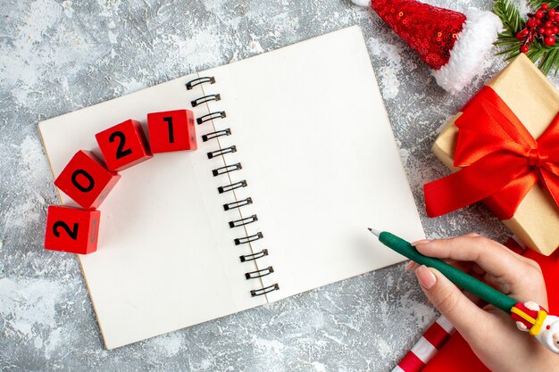 Bovenaanzicht notebook houtblokken kleine kerstmuts groen potlood in vrouwelijke hand op grijs witte tafel